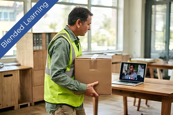 Worker in high-visibility vest carries a box while receiving online blended training on a laptop.