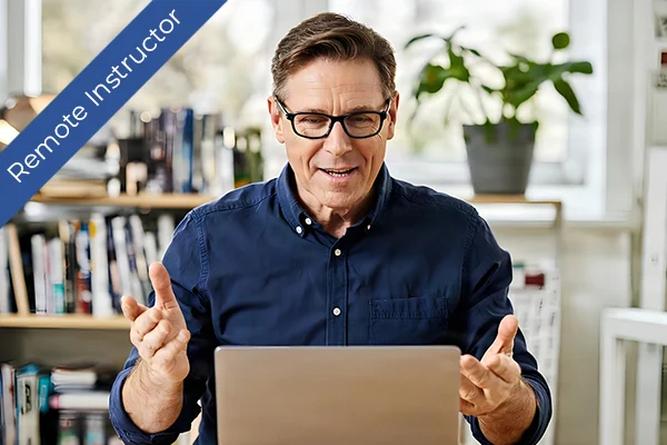 A mature remote instructor in a navy shirt uses a laptop, emphasizing virtual safety training.