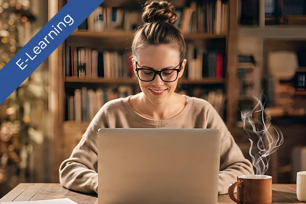 Woman working on a laptop in front of bookshelves. Steaming coffee mug nearby in a cozy study setting.
