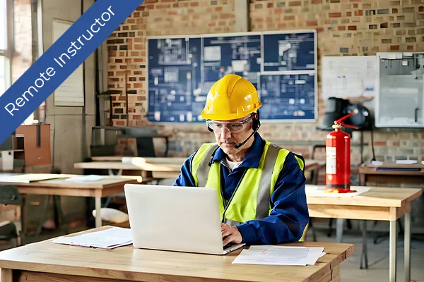 A man in a yellow hard hat using a laptop with a safety vest.